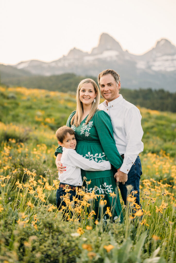 Family of three embracing in a sunflower field during a sunrise session in Grand Teton National Park