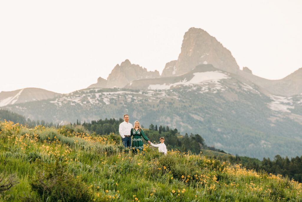 Grand Teton National Park family photographer capturing a sunrise session with parents and young son in front of the Teton mountain range and yellow sunflowers.