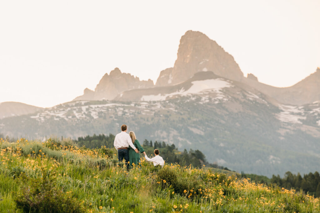Grand Teton National Park family photographer capturing a sunrise session with parents and young son in front of the Teton mountain range and yellow sunflowers.