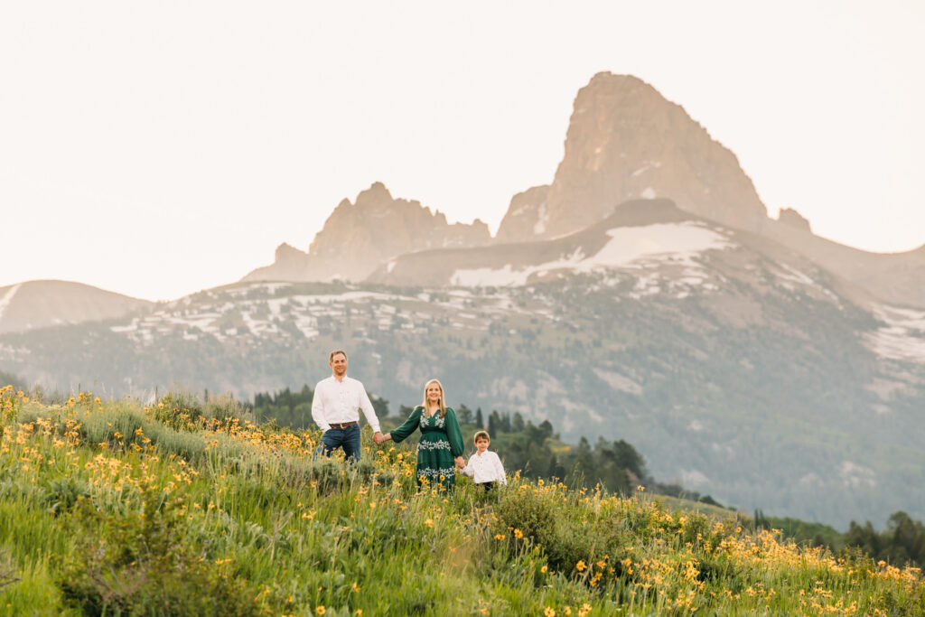 Grand Teton National Park family photographer capturing a sunrise session with parents and young son in front of the Teton mountain range and yellow sunflowers.