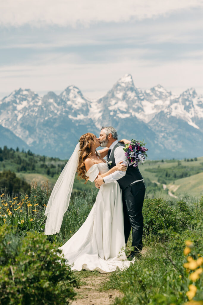 Bride and groom standing under The Wedding Tree with sweeping Teton mountain views