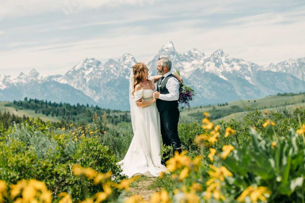 Bride and groom standing under The Wedding Tree with sweeping Teton mountain views