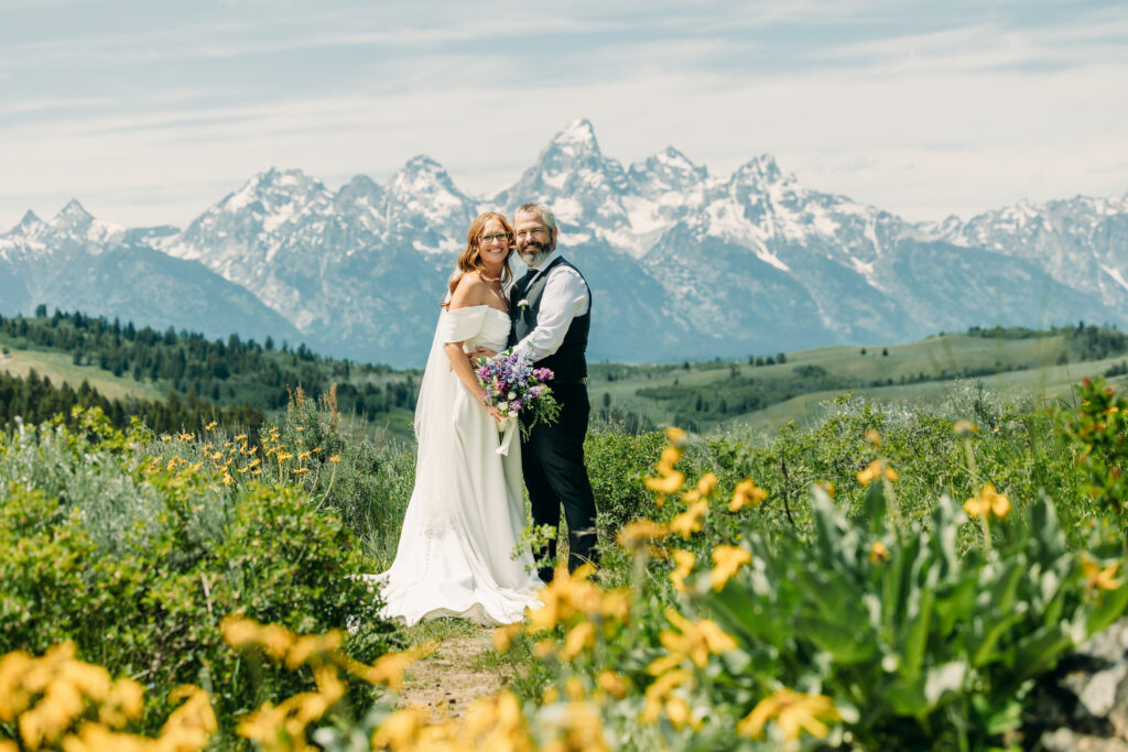Bride and groom standing under The Wedding Tree with sweeping Teton mountain views