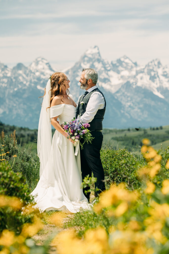Bride and groom standing under The Wedding Tree with sweeping Teton mountain views