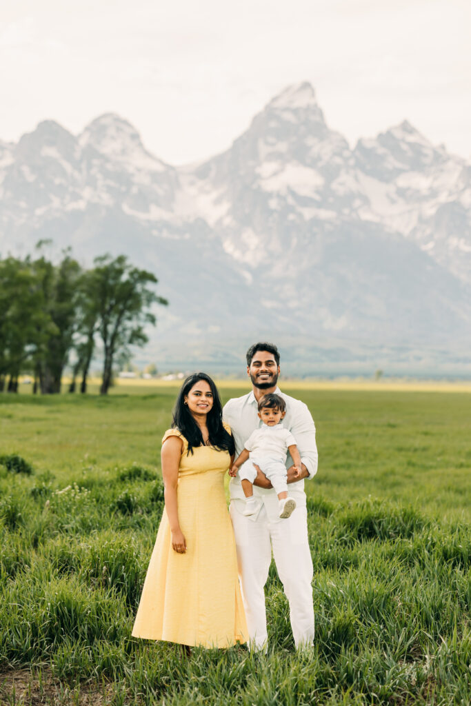 Family walking through green grass at Mormon Row Historic District with the Tetons behind them