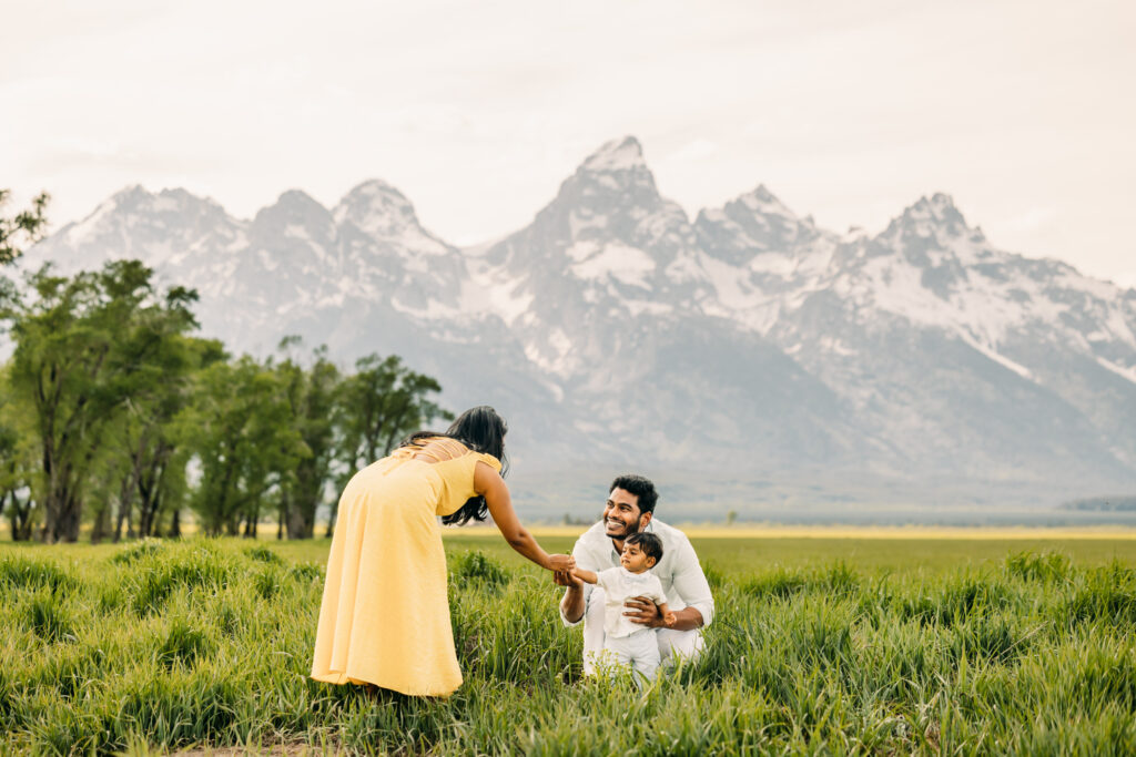 Family walking through green grass at Mormon Row Historic District with the Tetons behind them