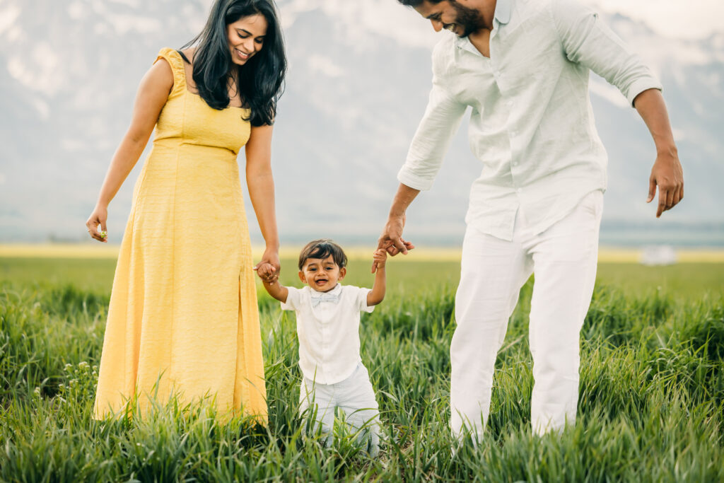 Family walking through green grass at Mormon Row Historic District with the Tetons behind them