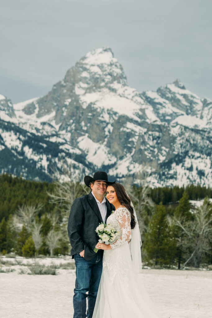 Bride and groom with Teton mountains during Jackson Hole wedding smiling at camera in wedding attire